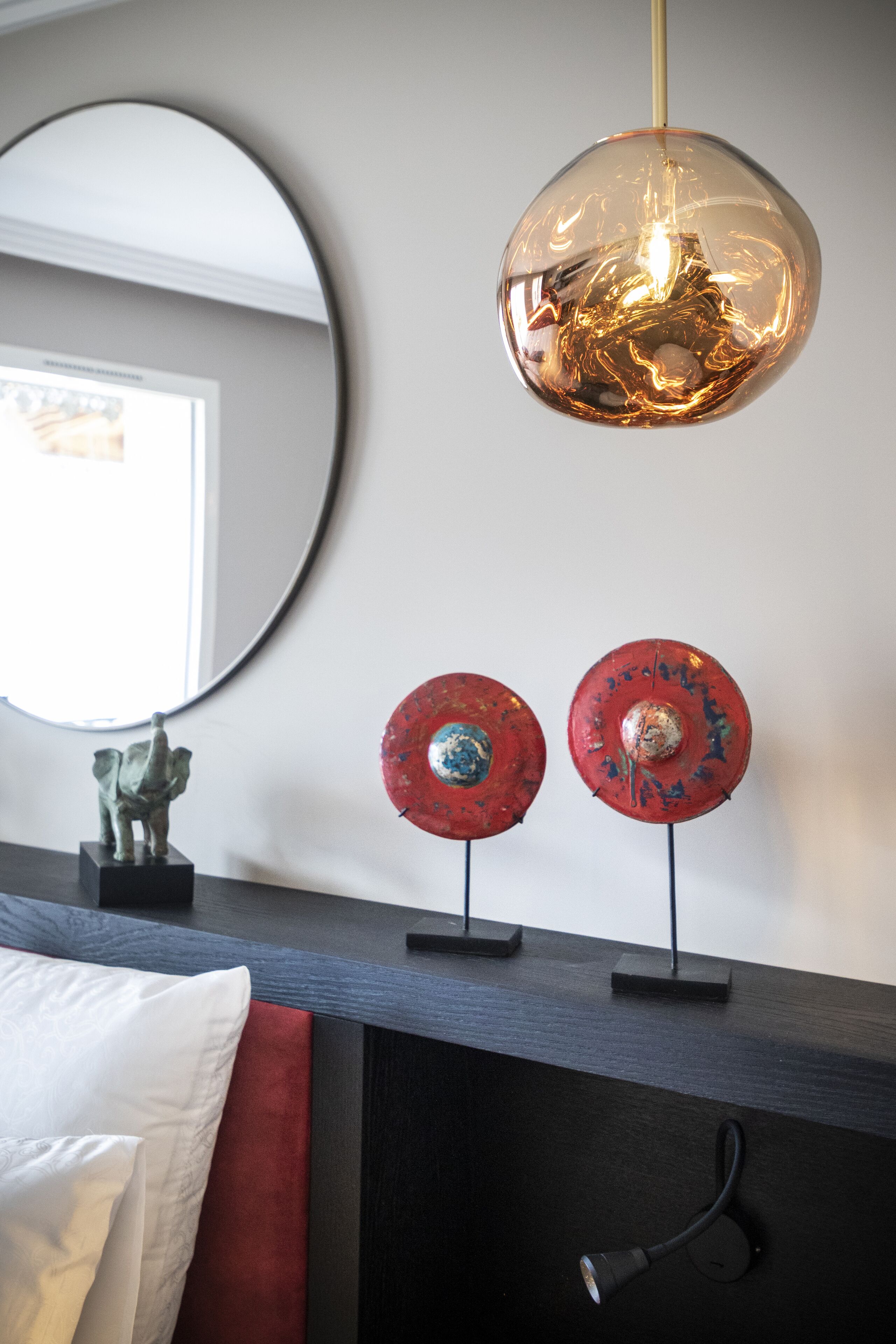 A modern room with a round mirror, a decorative light fixture, and two red wall decorations.