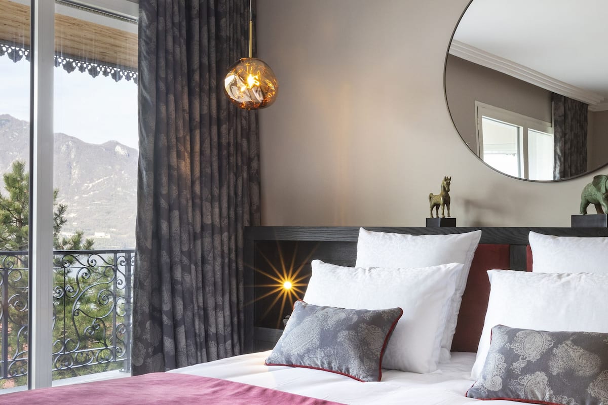 Ein Schlafzimmer mit einem großen Bett, einem runden Spiegel und Bergblick vom Balkon.
