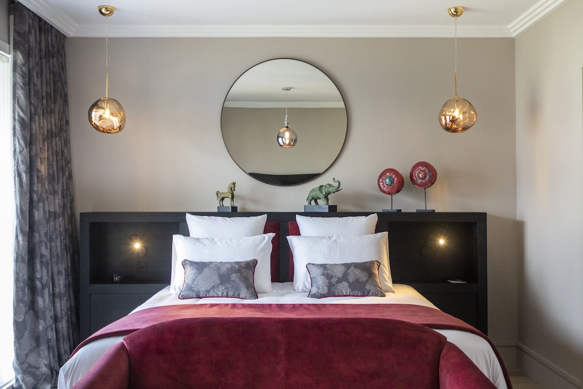Ein modernes Schlafzimmer mit einem großen Bett, zwei Nachttischen, einem runden Spiegel und zwei Pendelleuchten.