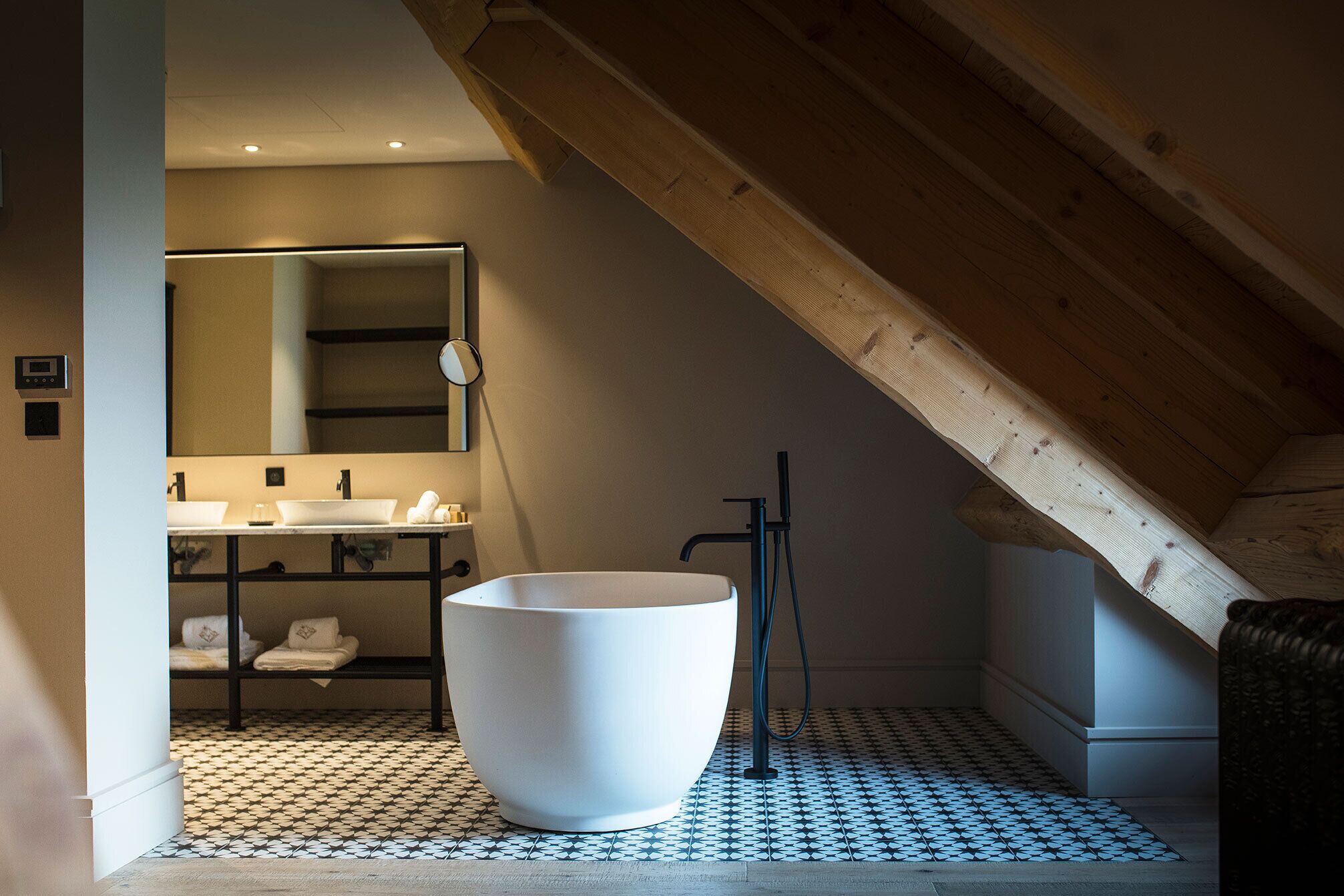 Un baño moderno con una bañera blanca grande, un lavamanos y un espejo. El piso tiene un diseño de baldosas con motivos.