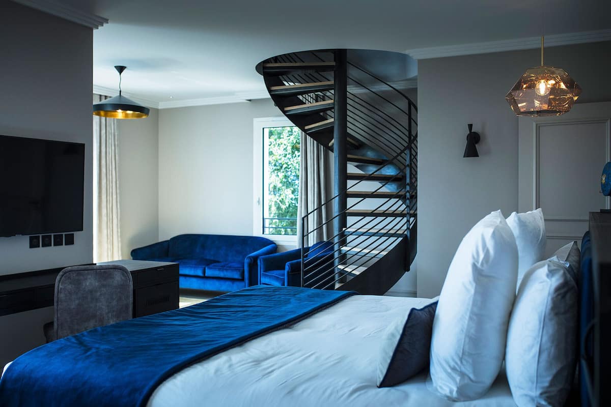 Ein modernes Schlafzimmer mit einer geschwungenen Treppe, einem Bett mit weißer und blauer Bettwäsche, einem blauen Sofa und einem Schreibtisch mit Stuhl.