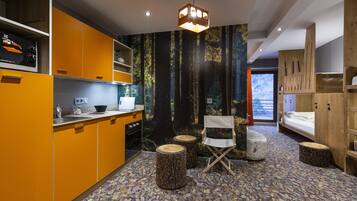 A compact, modern kitchen with orange cabinetry, a wooden dining area, and a forest-themed wall mural.