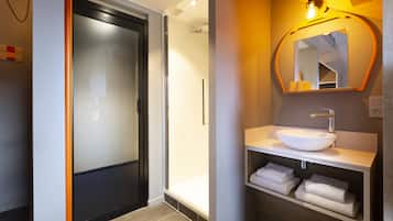 Un baño moderno con ducha de mampara de vidrio, un lavamanos blanco y un espejo con un marco original.