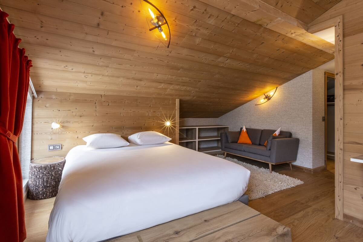 Une chambre avec un grand lit, un plafond en bois et un canapé gris.