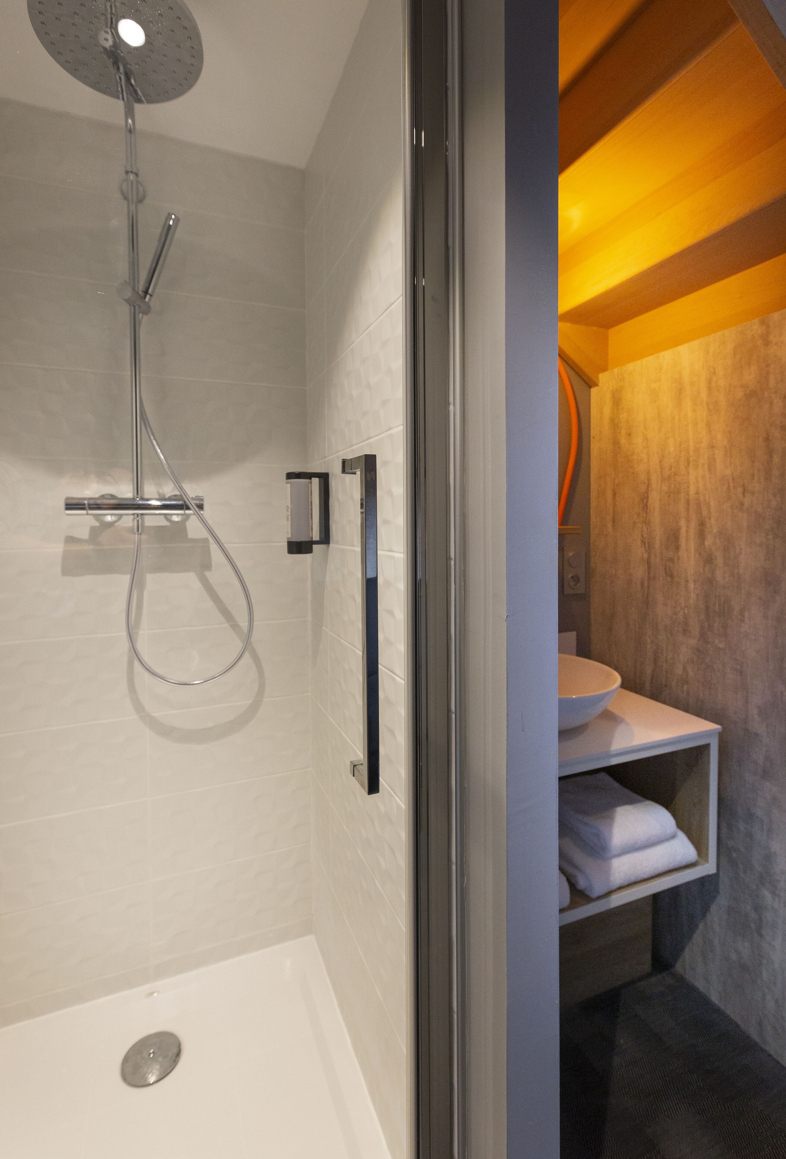 A modern bathroom with a glass-enclosed shower, a white sink, and a towel shelf.