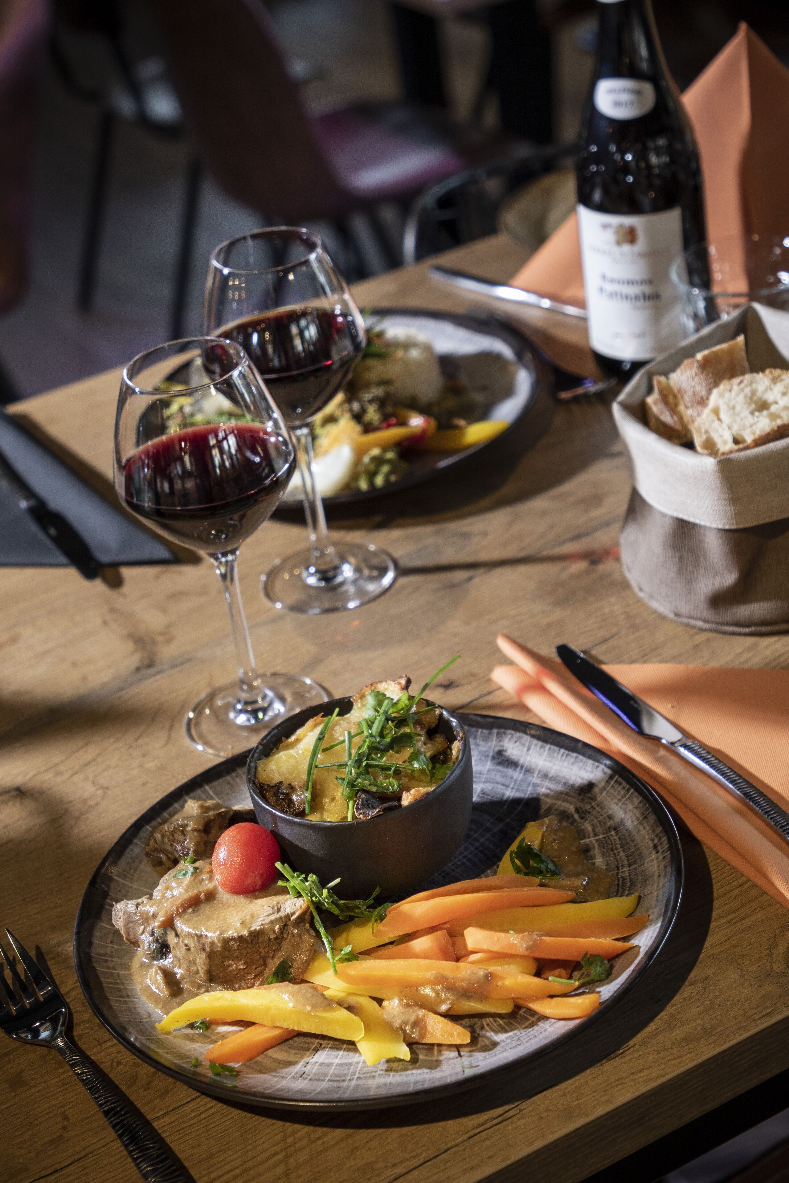 A dining table with plates of food, wine glasses, and a bottle of wine.