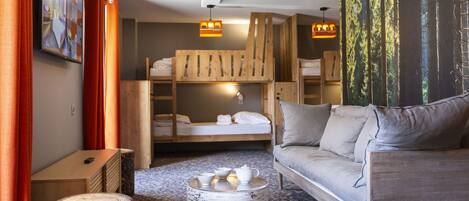 A modern room with a sofa, a bunk bed, a round wooden table, and a painting of a forest.