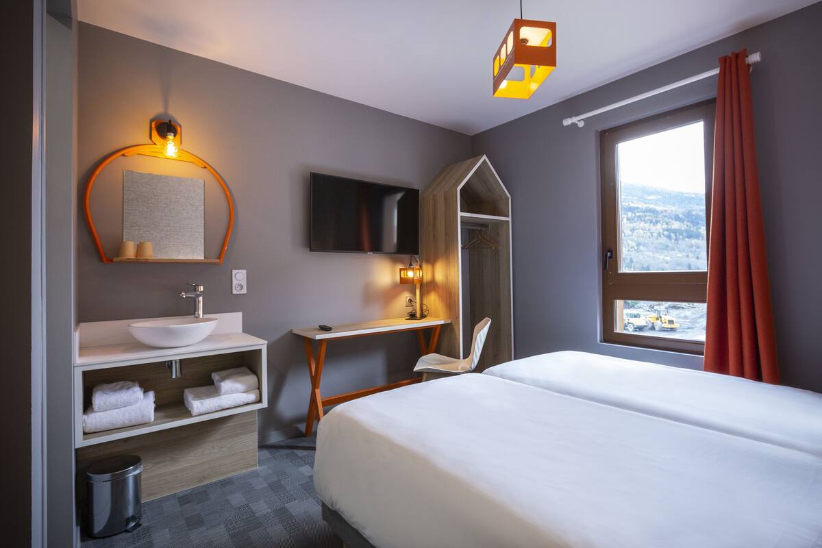 Une chambre d’hôtel comprenant un lit, un bureau, une salle de bain avec un lavabo et un miroir, et un téléviseur.