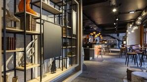 Un interior moderno con suelo de madera, estanterías metálicas con libros y objetos decorativos, y una zona de bar con taburetes y una barra.