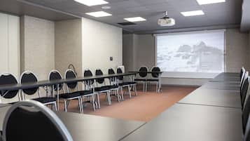 Un salón de conferencias con una larga mesa, varias sillas, una pantalla de proyector y piso alfombrado.