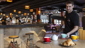 Un café con barra, taburetes de madera y una mesa con un croissant y tazas.