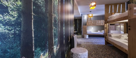 Una habitación con un mural de un bosque, literas, una mesa redonda y una alfombra estampada.