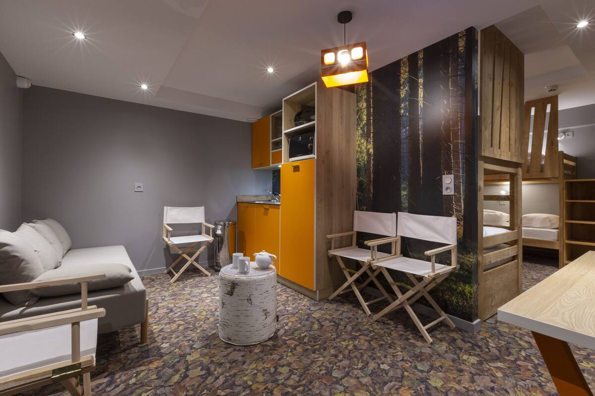 Une chambre moderne comprenant un canapé, une petite table avec une théière, une chaise pliante et un meuble en bois doté d’une étagère intégrée.