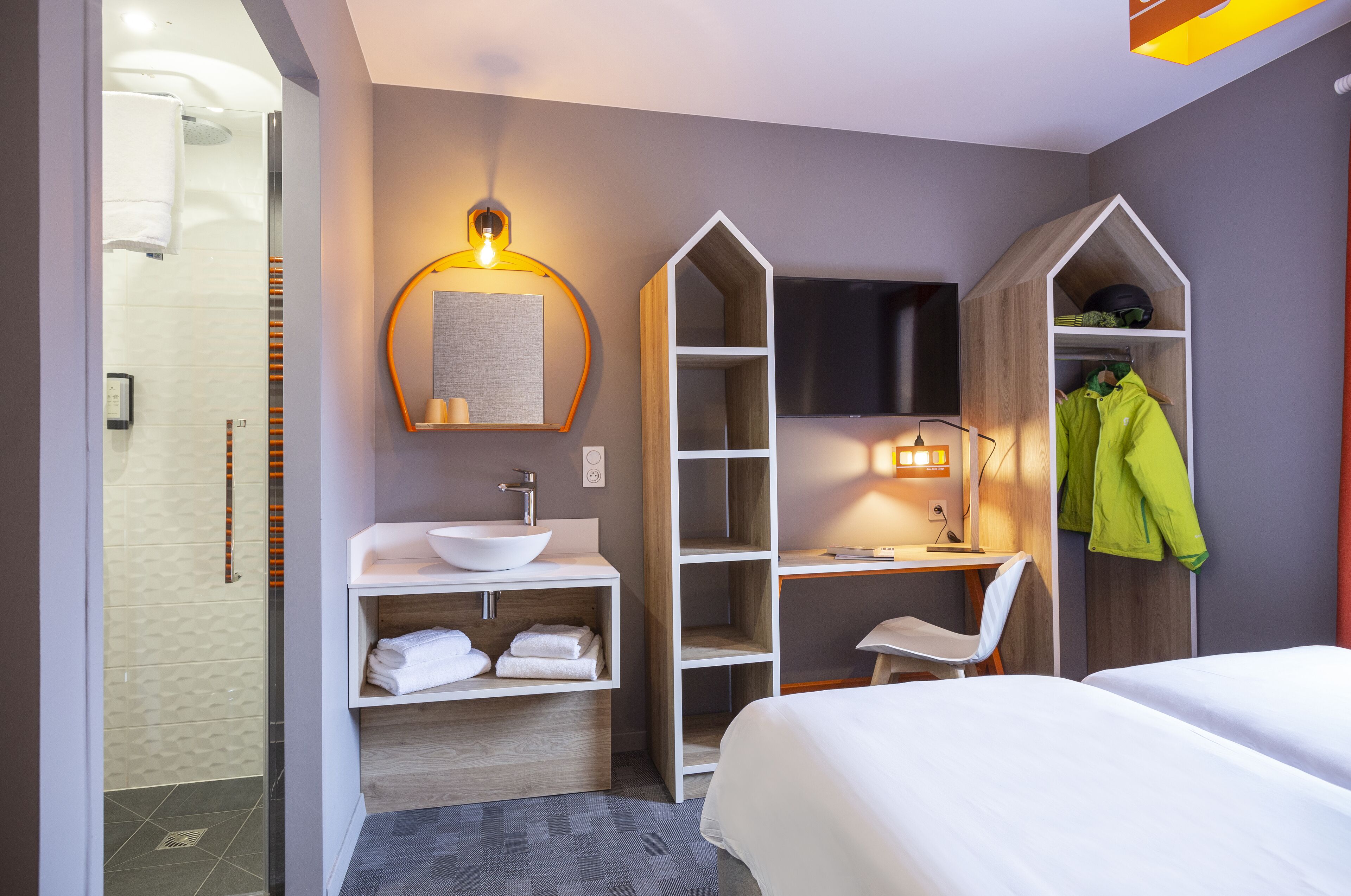 Ein modernes Hotelzimmer mit Bett, Schreibtisch, Waschtisch und begehbarem Kleiderschrank.