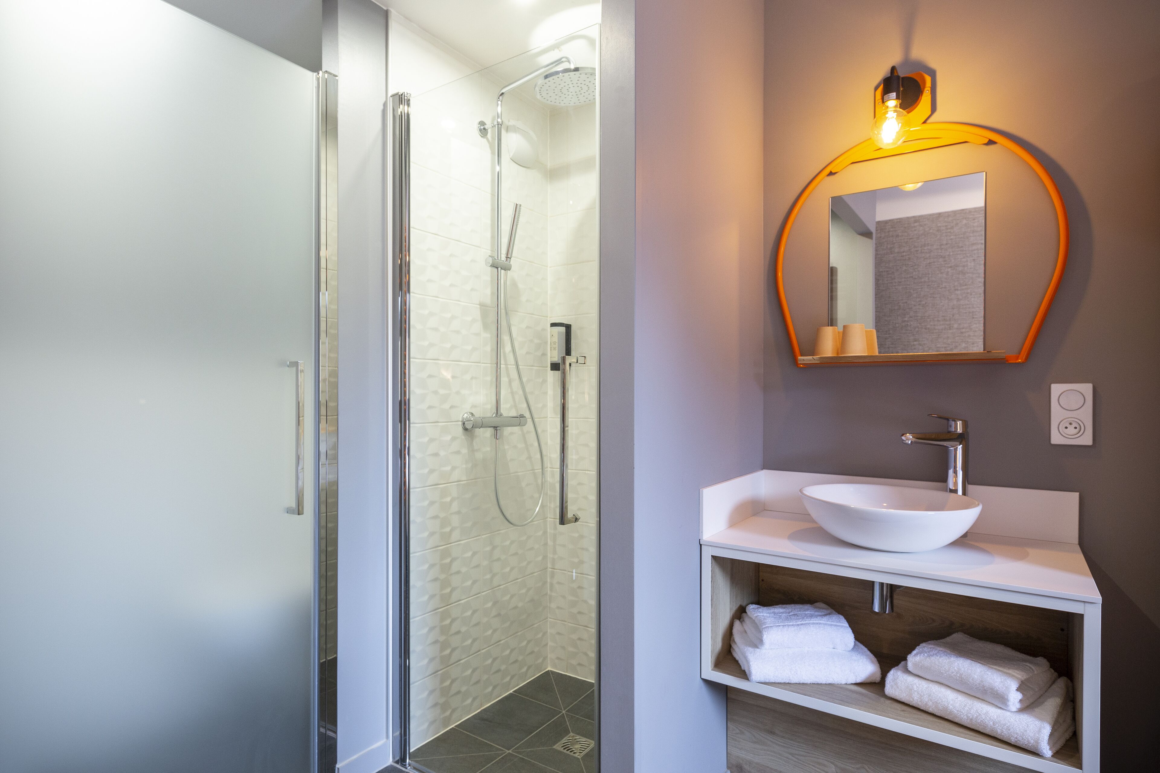 A modern bathroom with a glass-enclosed shower, a white sink with a bowl, and a mirror with a wooden frame.
