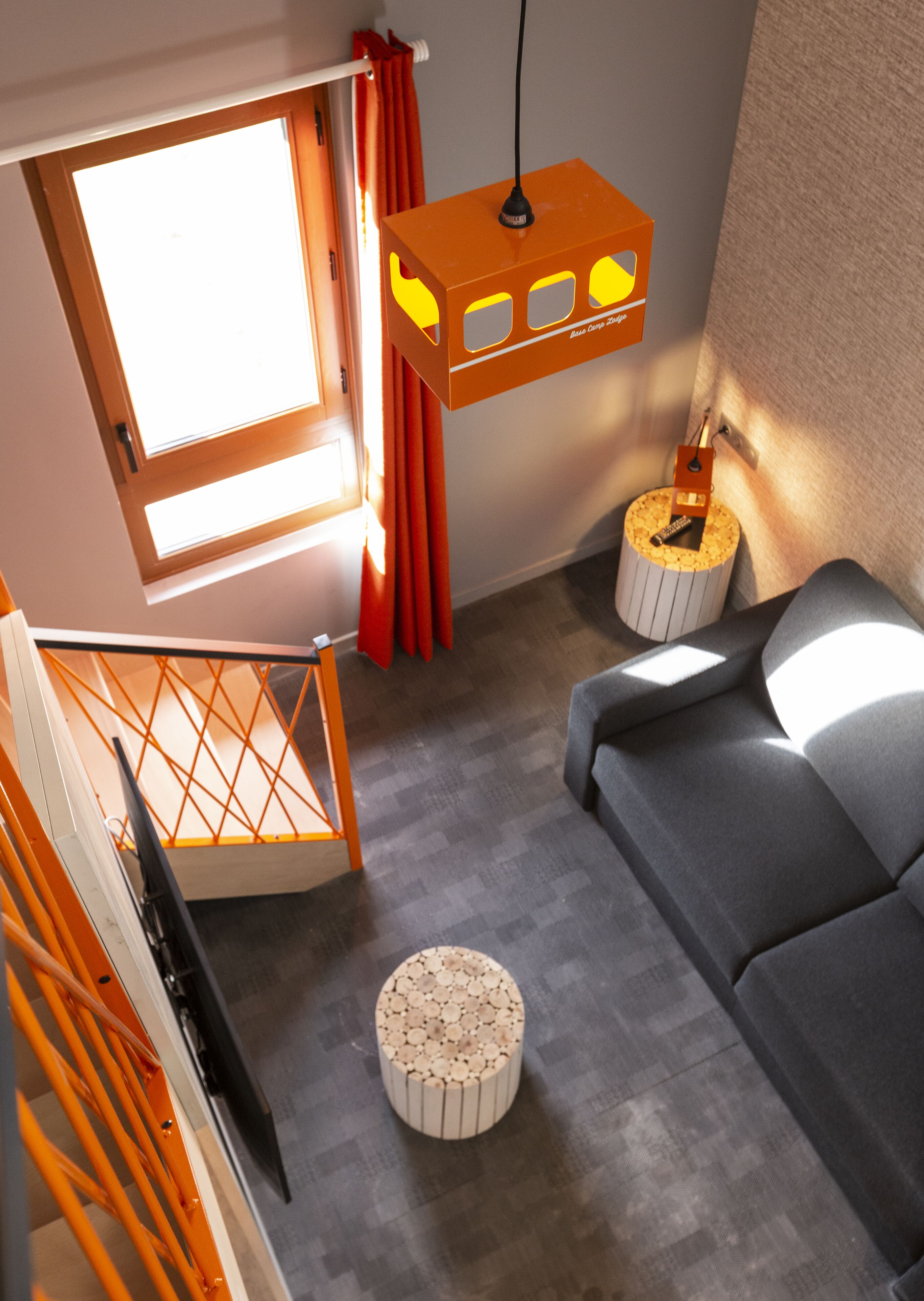 A modern living room with a grey sofa, a wooden staircase, and a hanging orange light fixture.