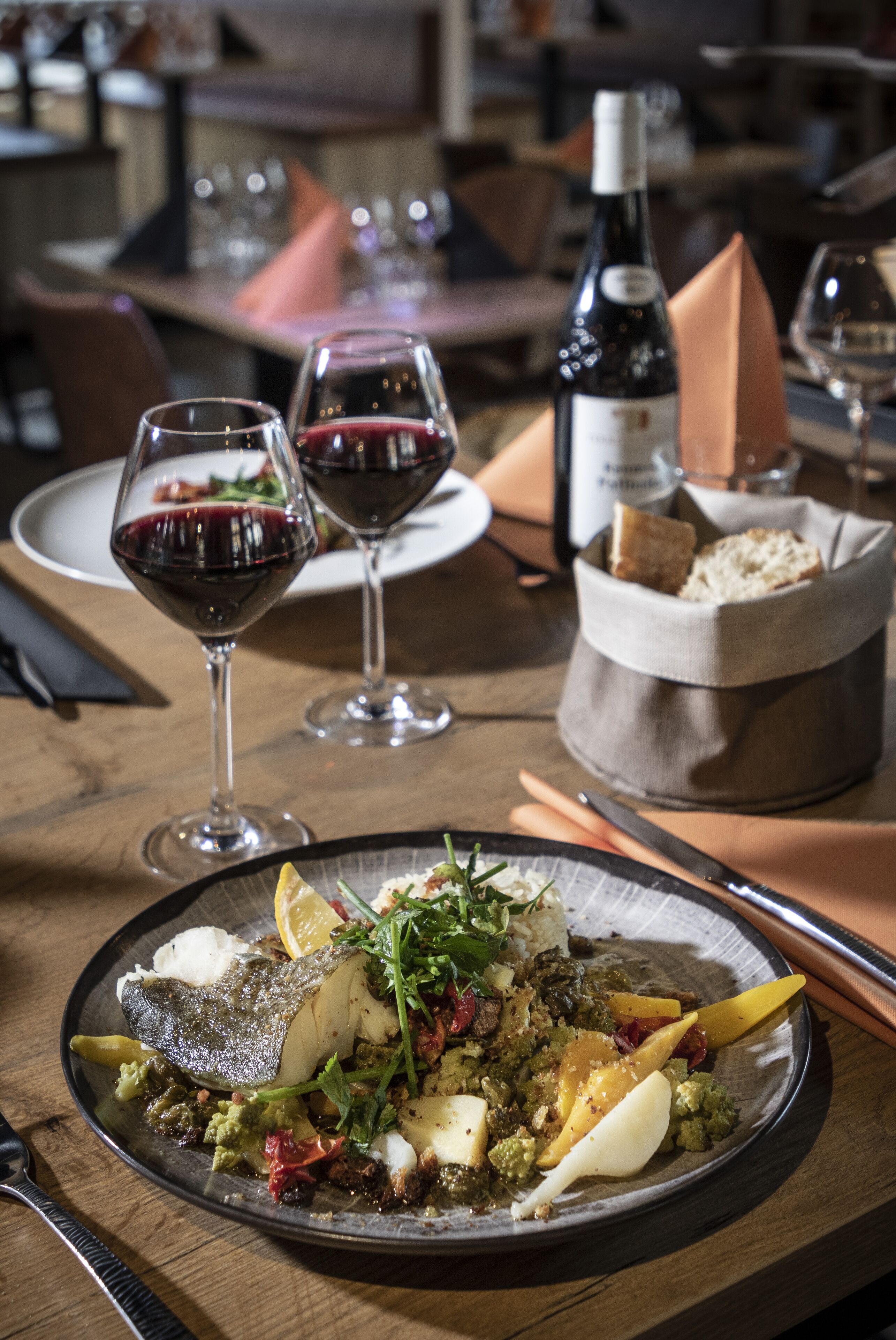 A dining table with a plate of food, wine glasses, and a bottle of wine.
