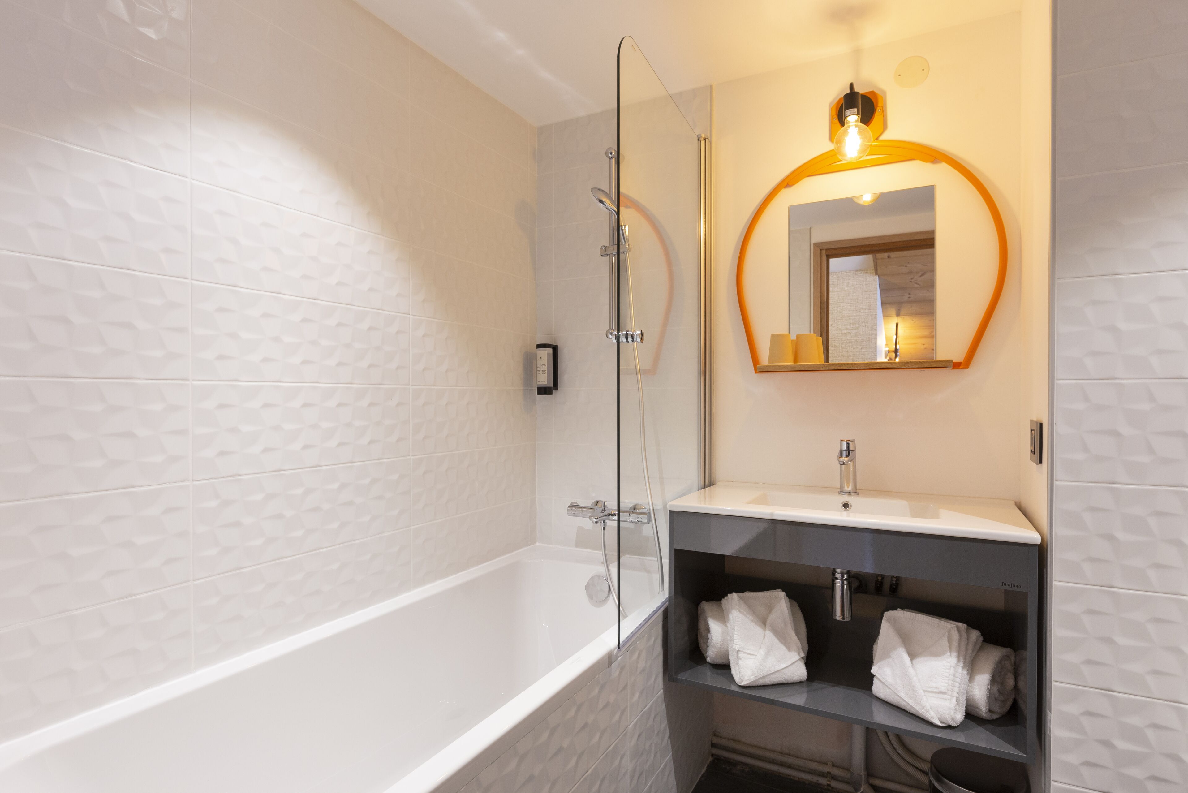 A modern bathroom with a glass-enclosed shower, a white bathtub, a vanity with a mirror, and shelves with towels.