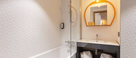 A modern bathroom with a glass-enclosed shower, a white bathtub, a vanity with a mirror, and shelves with towels.