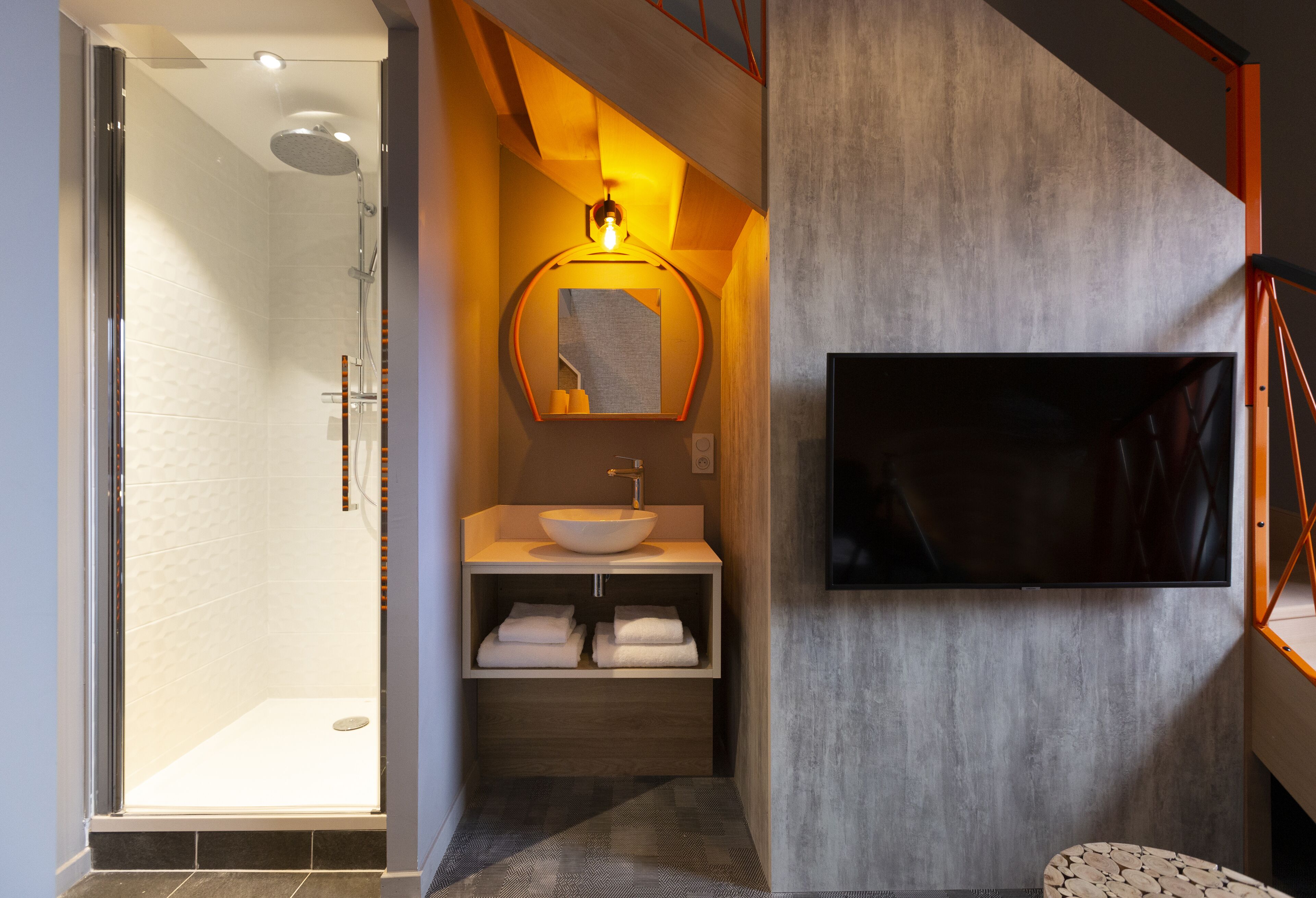 Ein modernes Badezimmer mit einer gläsernen Dusche, einem Holzwaschtisch mit Becken und einem flachbildfernseher an der Wand.