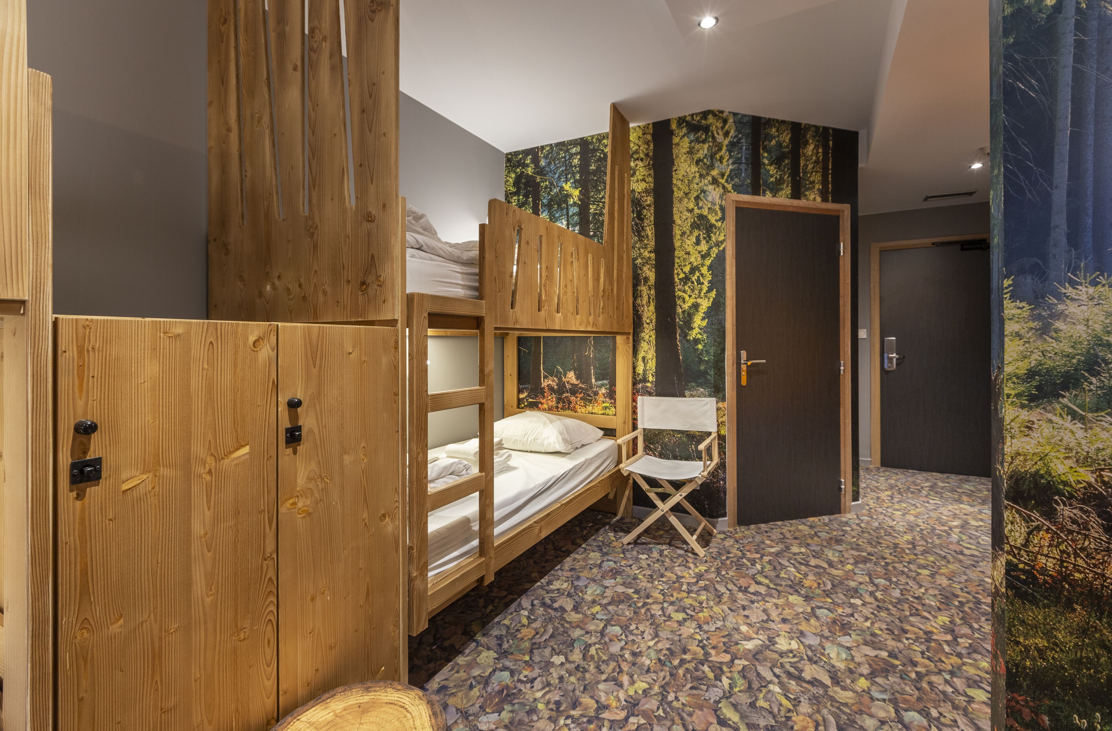 A room with bunk beds, a foldable chair, and a door leading to another room.