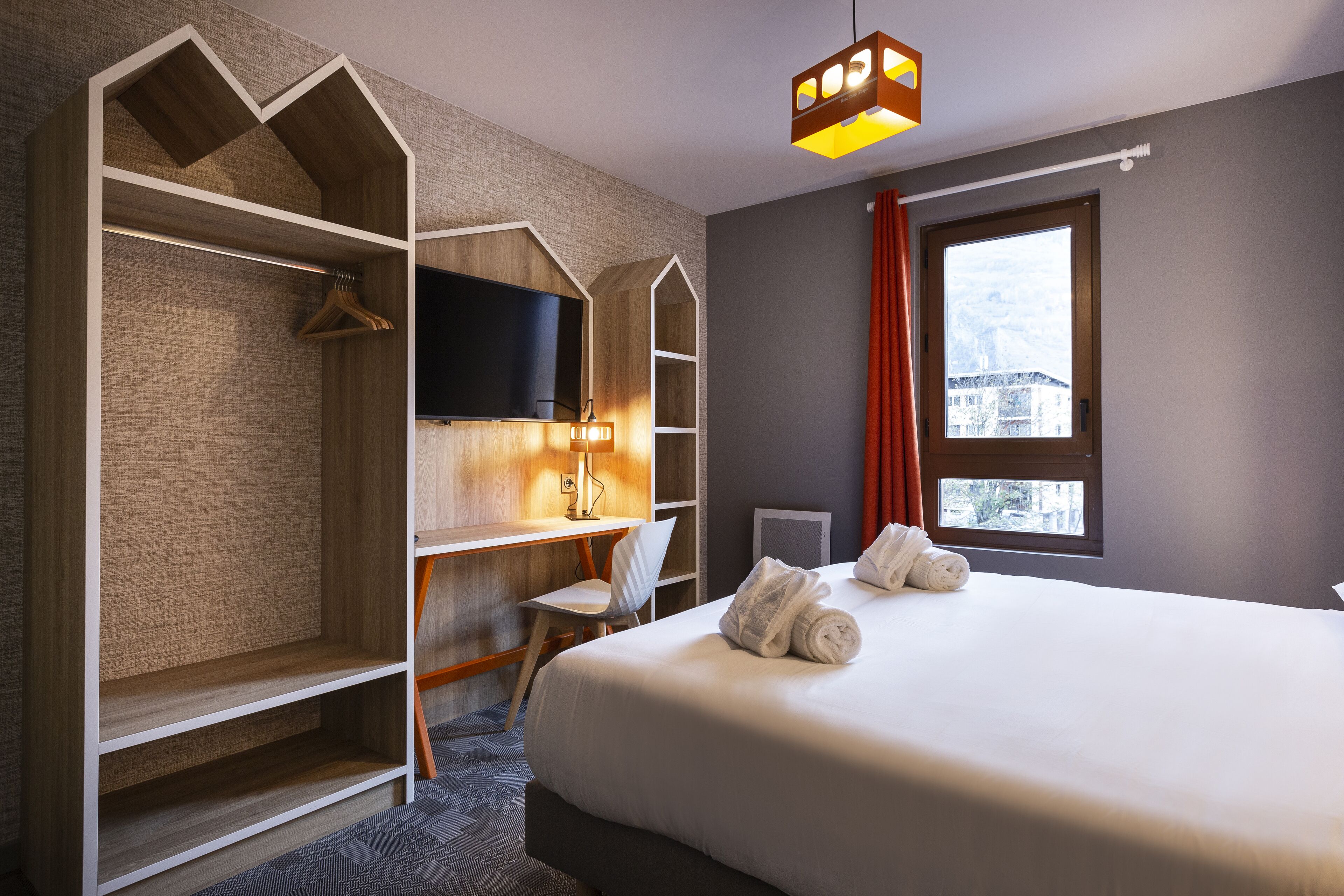 A hotel room with a bed, a desk, a TV, and a window with curtains.
