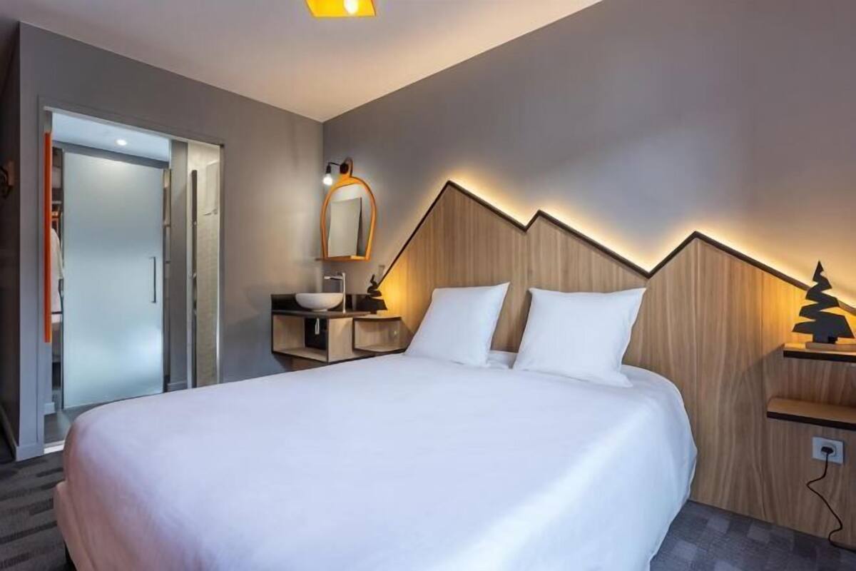 Une chambre d’hôtel avec un grand lit, une table de chevet avec une lampe, un miroir et une tête de lit en bois.