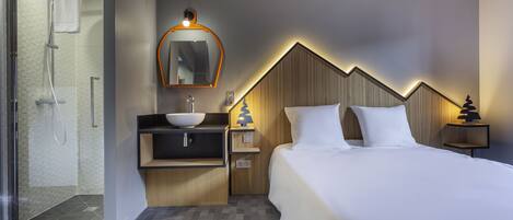 A modern hotel room with a bed, bedside tables, a vanity with a mirror, a shower area, and a wooden accent wall.