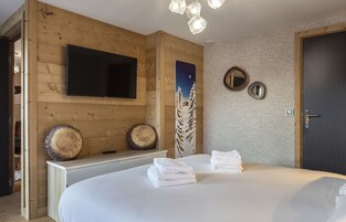 A modern hotel room with a wooden wall, a flat-screen TV, a bed with neatly folded towels, and a night sky poster.