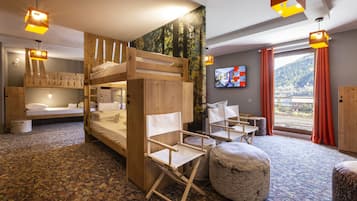 A room with bunk beds, a foldable chair, ottomans, a television, and a view of a mountain.