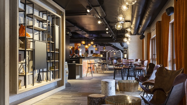 Un interior moderno con un largo pasillo que conduce a un comedor, con suelo de madera, taburetes de abedul y una zona de bar.