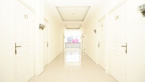 Een lichte, witte gang met deuren met daarop C7, C6 en C8, die leidt naar een kamer met een roze muur en een raam.