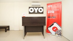 Een receptiebalie met een houten bureau, een wandairconditioner en een reclamebanner voor OYO Hotels.