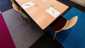 Kokouspöytä tuoleineen, valkoisine aluslautasineen ja vihreine kynineen.