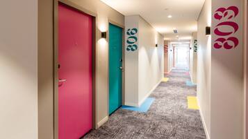 A hotel corridor with colorful doors, carpeted flooring, and wall-mounted light fixtures.