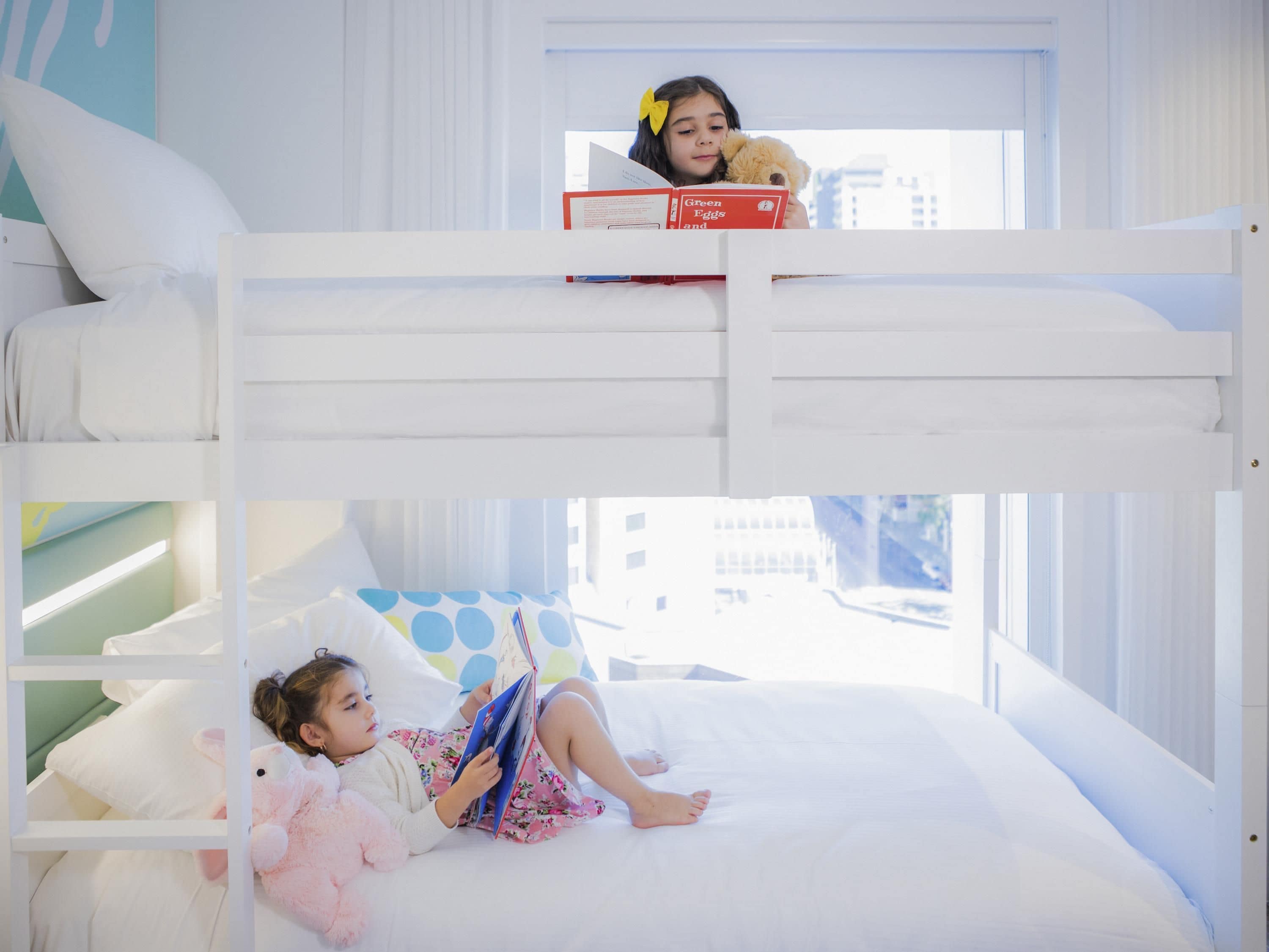 Habitación con literas y vista a la ventana, una cama con almohada de lunares y un niño leyendo un libro.