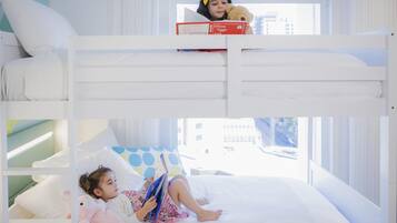 Habitación con literas y vista a la ventana, una cama con almohada de lunares y un niño leyendo un libro.