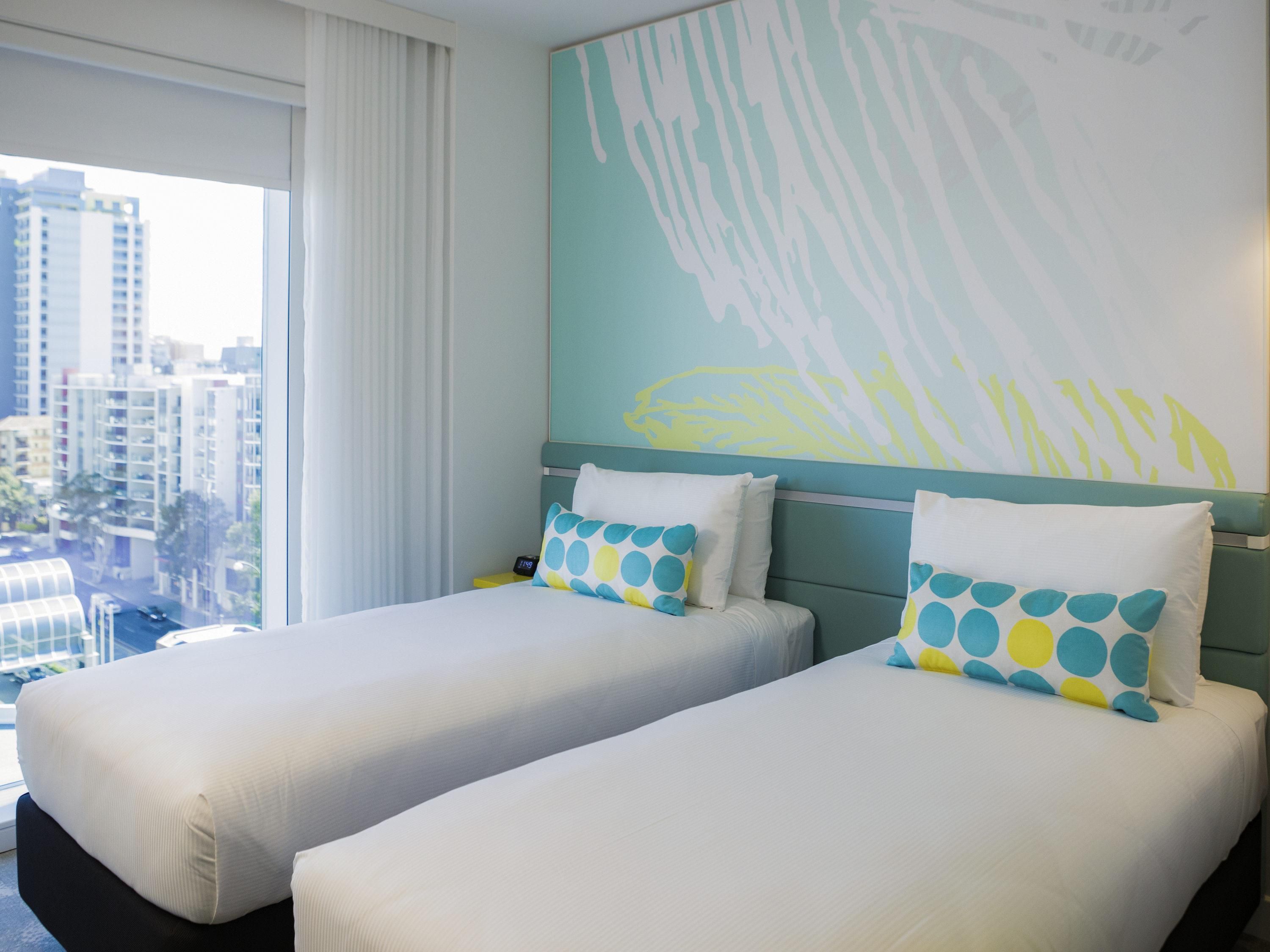Una habitación de hotel con dos camas, un ventanal con cortinas y vistas a la ciudad.