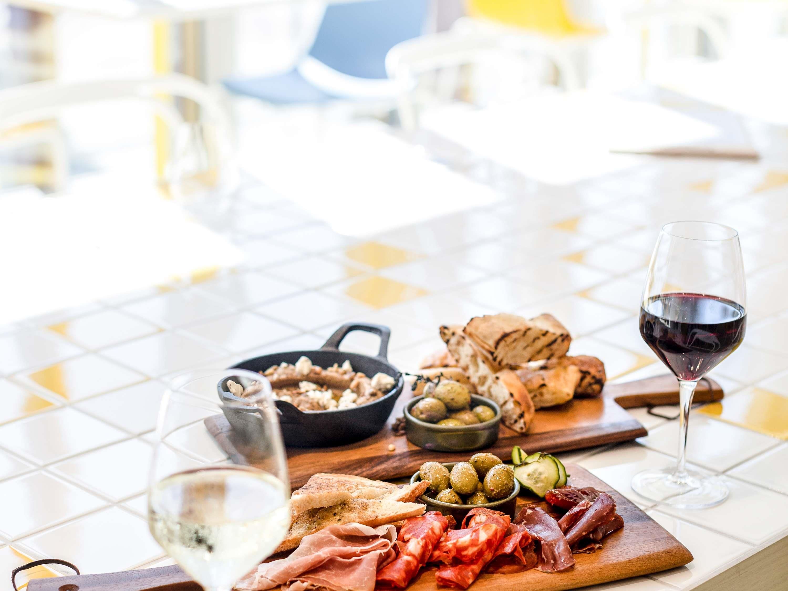 Una mesa de comedor con una variedad de alimentos, incluyendo aceitunas, pan y carnes, junto con una copa de vino tinto.