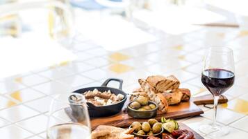 Une table à manger dressée avec une variété d’aliments, notamment des olives, du pain et de la viande, ainsi qu’un verre de vin rouge.