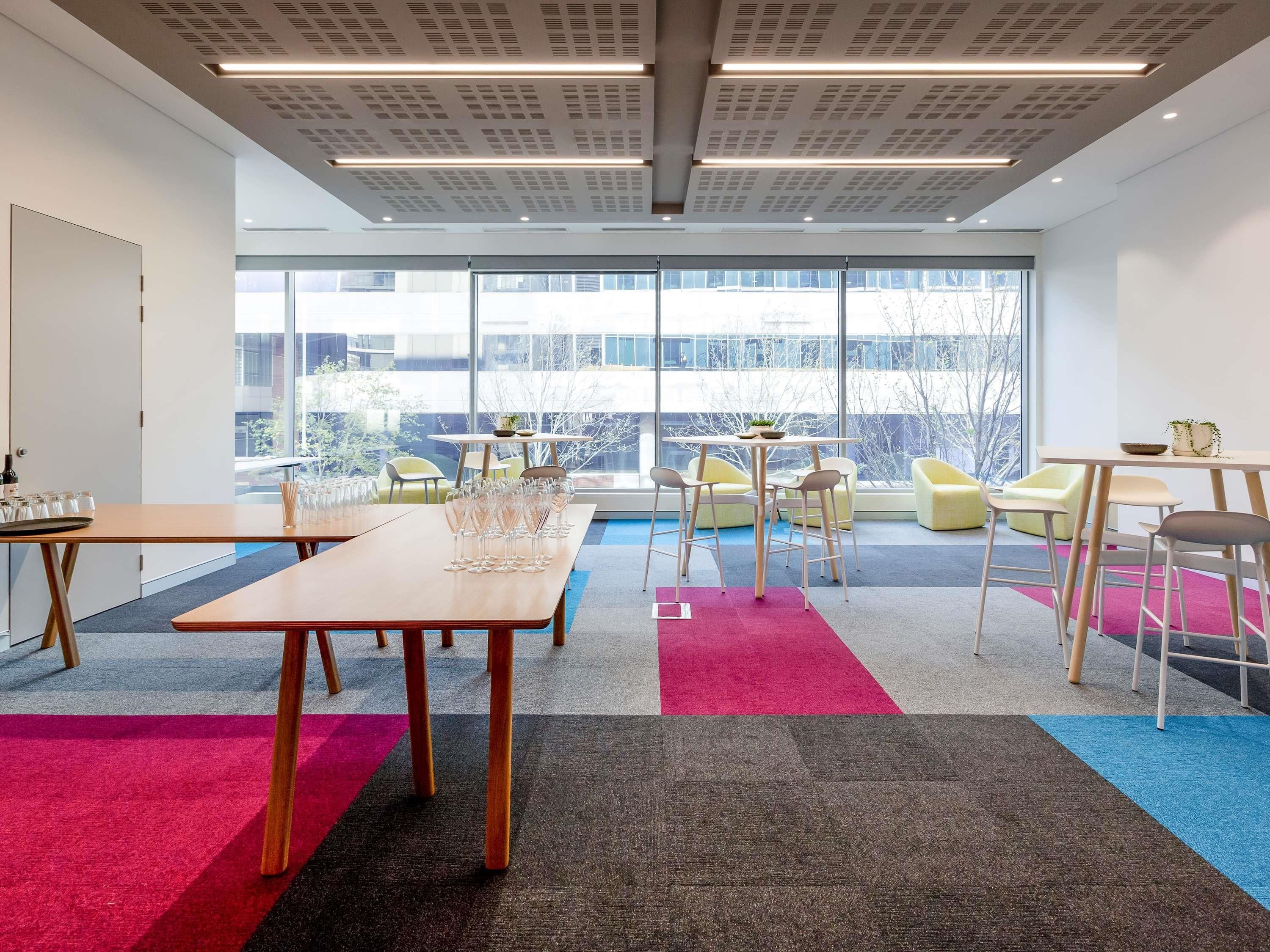Un espace de bureau moderne avec de grandes fenêtres, une table en bois et une moquette colorée.