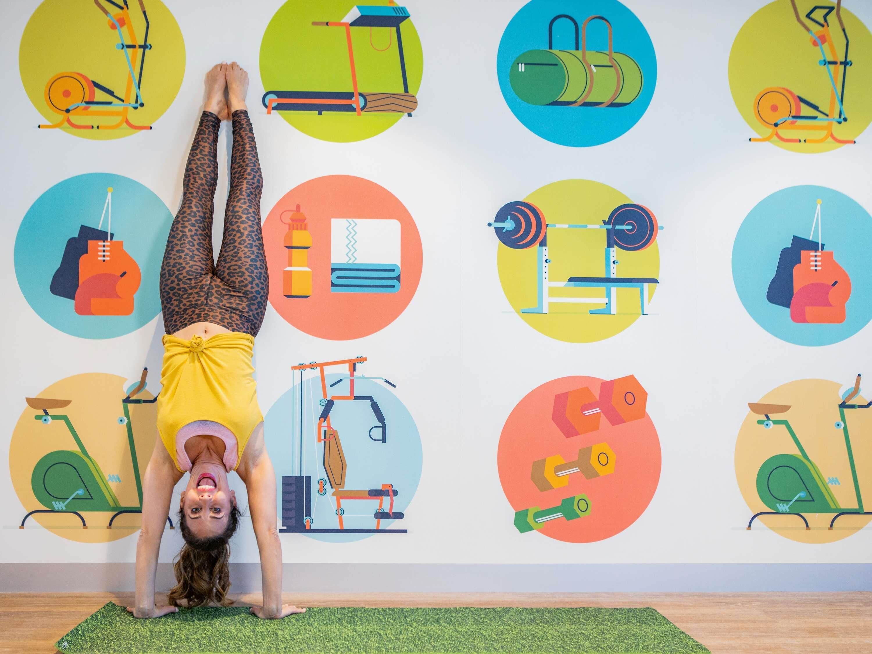 A person performing a yoga pose on a mat with a wall displaying various fitness equipment illustrations.