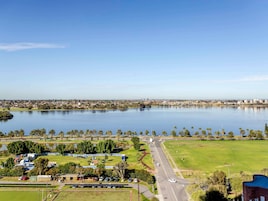 Un'ampia distesa d'acqua con sullo sfondo un paesaggio urbano, una strada con veicoli e una zona verde con alberi e edifici.