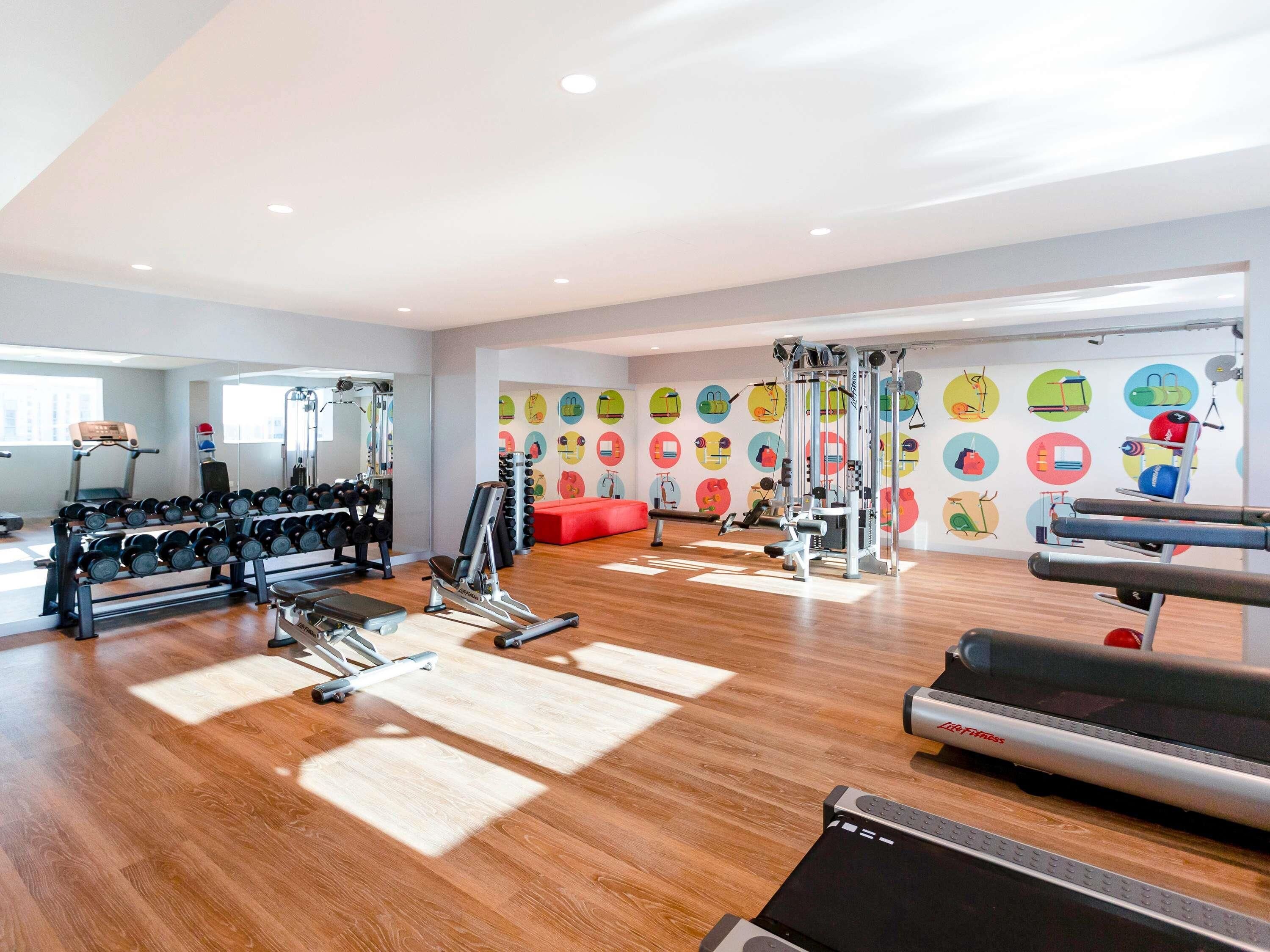 A gym with exercise equipment, a treadmill, and a wall with colorful circular designs.