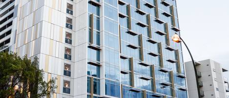 Un edificio moderno de gran altura con fachada de vidrio y una sección de fachada de madera al nivel de la calle.