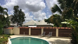 Una piscina con una escalera de metal, rodeada por un muro de ladrillo bajo y palmeras.
