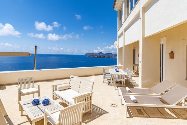 A balcony with white furniture, including chairs and a table, overlooking a clear blue sea with distant land. - House with beautiful views to the sea, front line with pool and several terraces (El Toro)