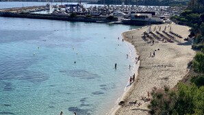 En hamn vid kusten med båtar, en sandstrand och ett bergigt landskap i bakgrunden.