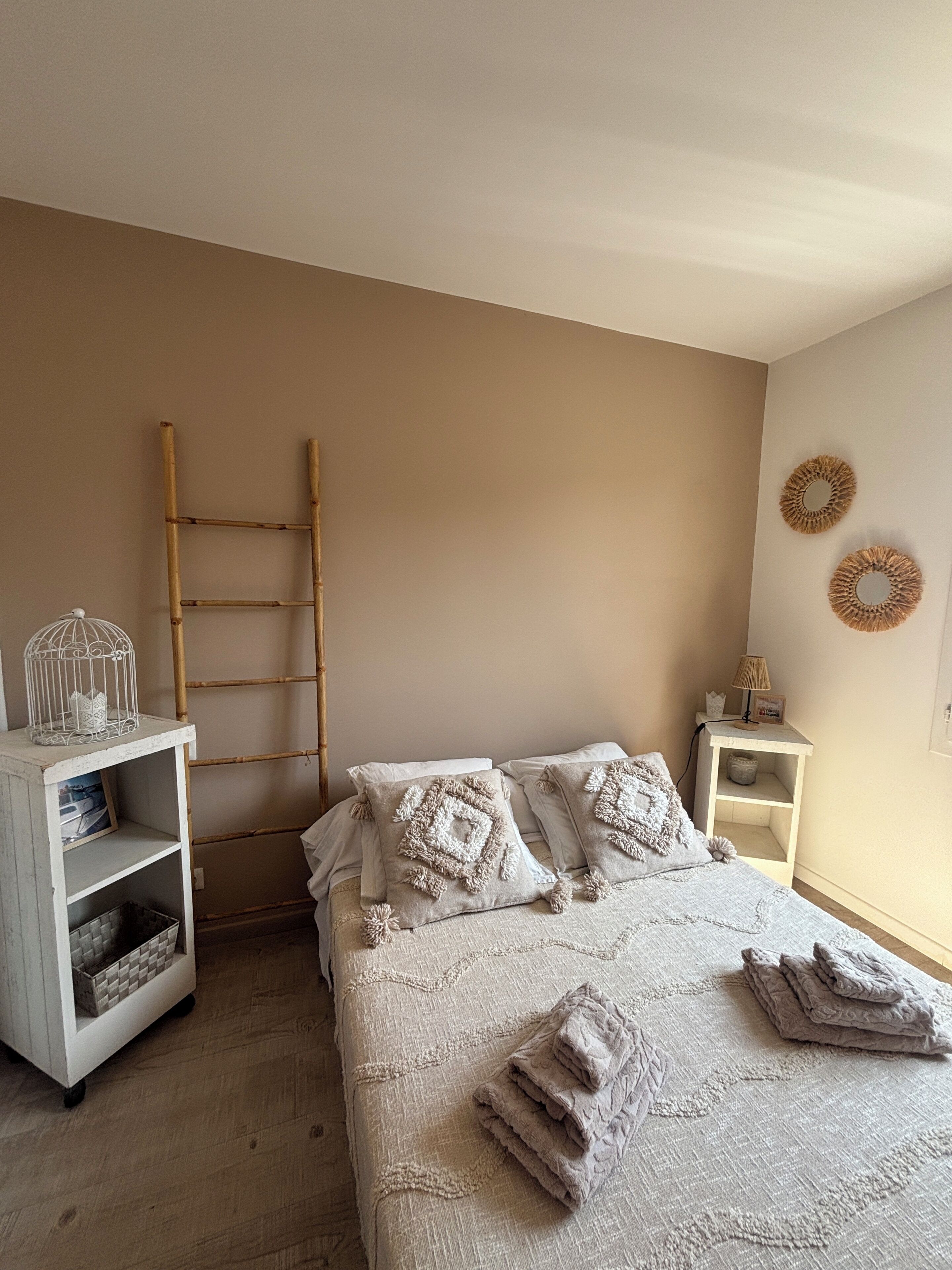 Een slaapkamer met een bed, nachtkastje, plank, ladder en decoratieve wandobjecten.