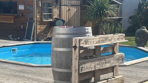 Une terrasse en bois avec une piscine, un tonneau en bois et une enseigne sur laquelle on peut lire « BAR-A-PETANQUE ».